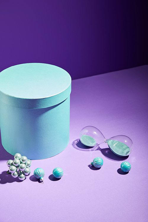 blue gift box and decorative baubles and hourglass on purple background