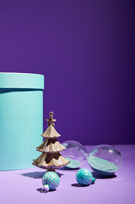 blue gift box and decorative Christmas tree with baubles and hourglass on purple background