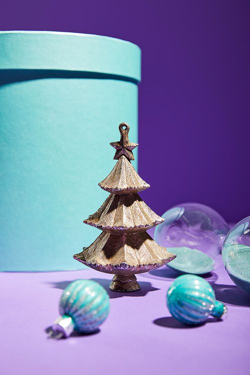 selective focus of decorative Christmas tree with baubles near hourglass and blue gift box on purple background