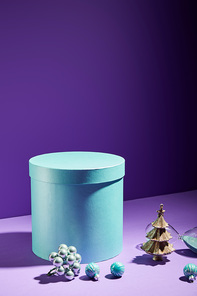 blue gift box and decorative Christmas tree with baubles near hourglass on purple background