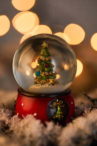 decorative snowball with christmas tree standing in snow with golden lights bokeh