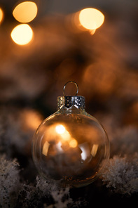 transparent christmas ball on spruce branches in snow with blurred yellow lights in dark