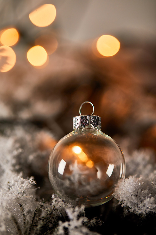 transparent christmas ball on spruce branches in snow with blurred yellow lights