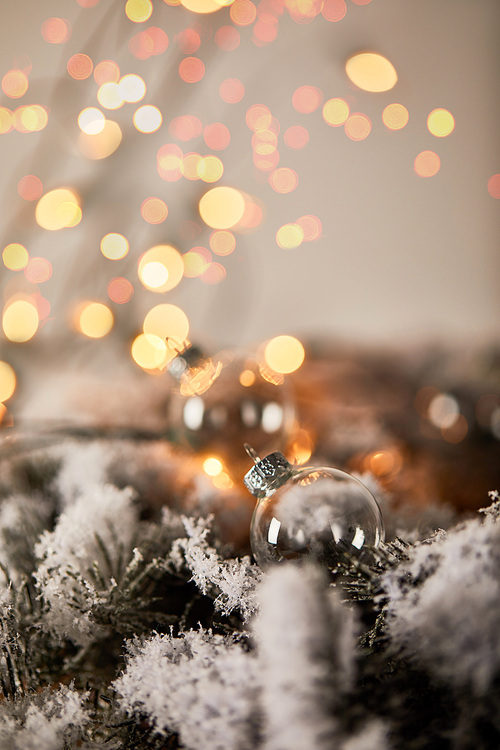 transparent christmas balls on spruce branches in snow with blurred yellow lights