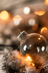 one transparent christmas ball on spruce branches in snow with blurred yellow lights
