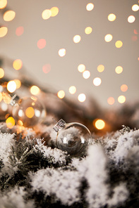 transparent christmas balls on spruce branches in snow with blurred yellow lights