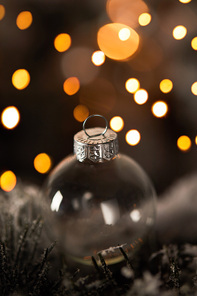 close up of transparent christmas ball on spruce branches in snow with yellow lights bokeh
