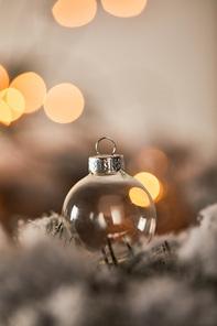 transparent christmas ball on spruce branches in snow with lights bokeh