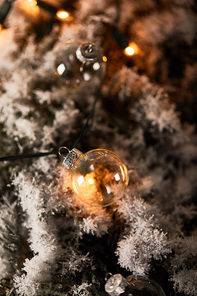 selective focus of transparent christmas balls and yellow lights on spruce branches in snow