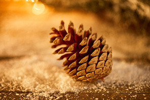 one pine cone on wooden table in snow and christmas lights bokeh