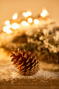 pine cone on wooden table with spruce branches in snow and christmas lights bokeh