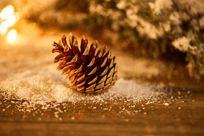 decorative pine cone on wooden table with spruce branches in snow and blurred christmas lights