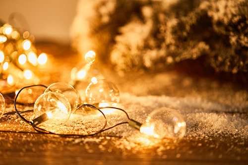 christmas garland with transparent light bulbs on wooden surface with spruce branches in snow