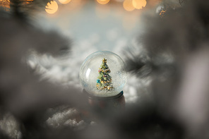 selective focus of little snowball with christmas tree standing in snow with spruce branches and lights bokeh