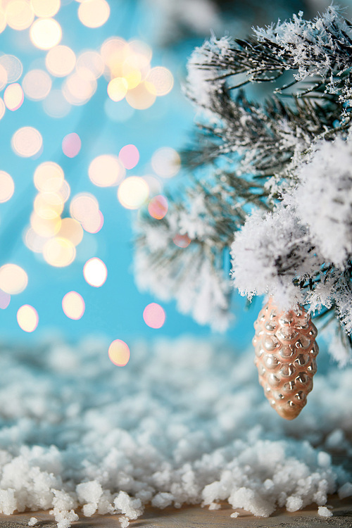 spruce branches in snow with christmas ball pine cone and blurred lights on blue