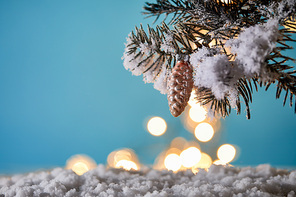 christmas tree in snow with decorative pine cone and christmas lights bokeh on blue