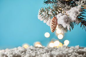 christmas tree branches in snow with decorative pine cone and christmas lights bokeh on blue