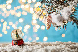 christmas tree in snowball standing on blue with spruce branches in snow and lights bokeh