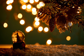 little snowball with christmas tree standing in snow with spruce branches, christmas ball and blurred lights at night