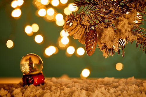 snowball with christmas tree standing in snow with spruce branches, christmas ball and blurred lights at night