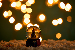 little snowball with christmas tree standing in snow with blurred lights at night