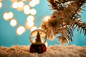 decorative christmas tree in snowball standing on blue with spruce branches in snow and blurred lights