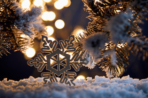 close up of decorative snowflake with spruce branches in snow with blurred christmas lights