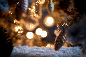 close up of christmas tree with decorative christmas balls on snow with blurred lights in dark