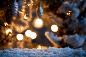 close up of spruce branches in snow with christmas balls and lights bokeh at night