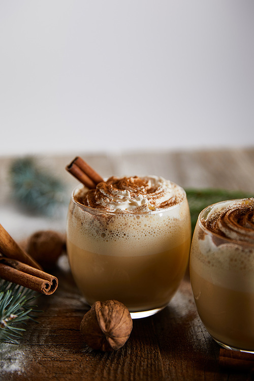 delicious eggnog cocktail with whipped cream, cinnamon sticks and wallnuts on wooden table isolated on grey