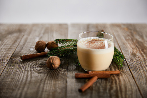 delicious eggnog cocktail near wallnuts, spruce branch and cinnamon sticks on wooden table isolated on grey