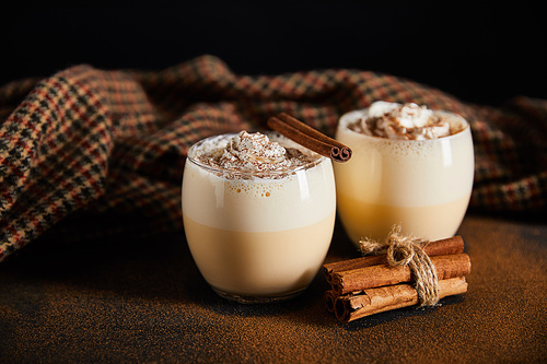 delicious eggnog cocktail, cinnamon branches and checkered cloth on table covered with cinnamon powder isolated on black
