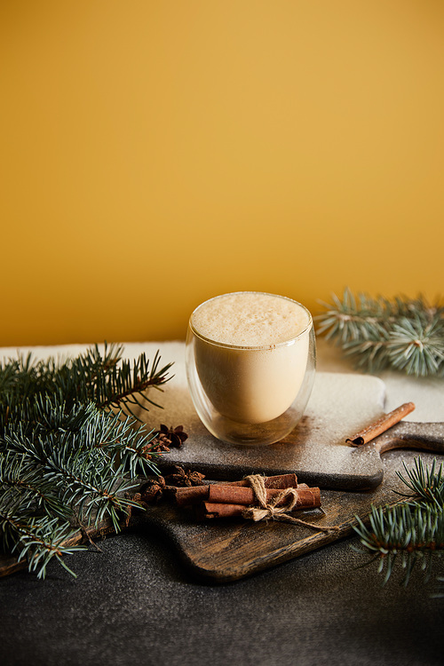 traditional eggnog cocktail on chopping board covered with sugar powder, spruce branches and cinnamon sticks on orange background