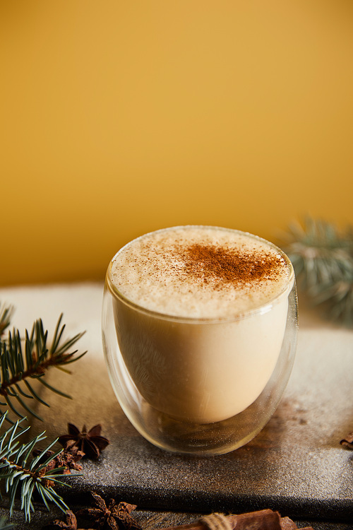 traditional eggnog cocktail with cinnamon near spruce branches and scattered sugar powder on orange background