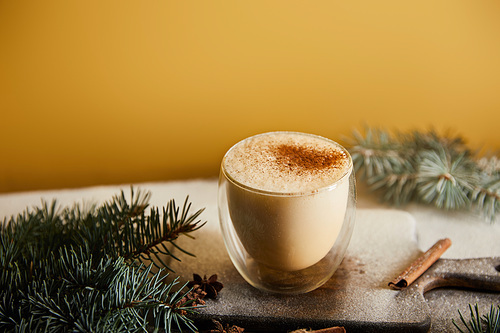 traditional eggnog cocktail on chopping board, spruce branches, cinnamon sticks, straw, and scattered sugar powder on orange background