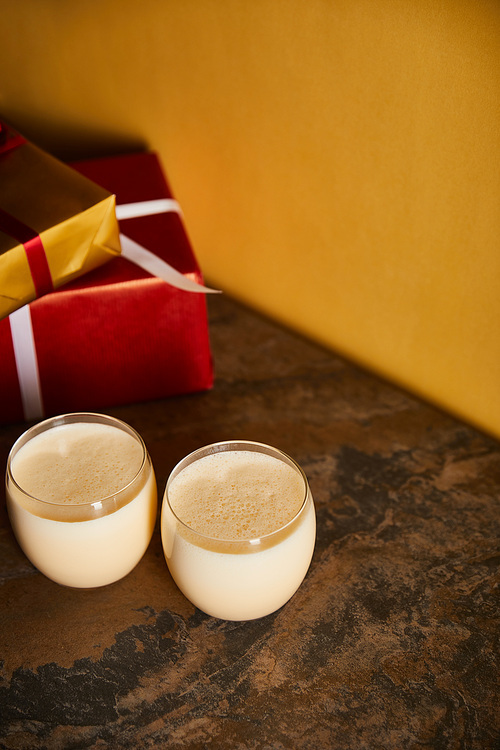 delicious eggnog cocktail and gift boxes on dark marble table near orange wall