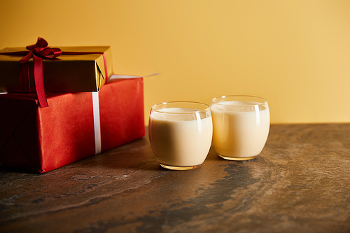delicious eggnog cocktail and gift boxes on dark marble table isolated on orange