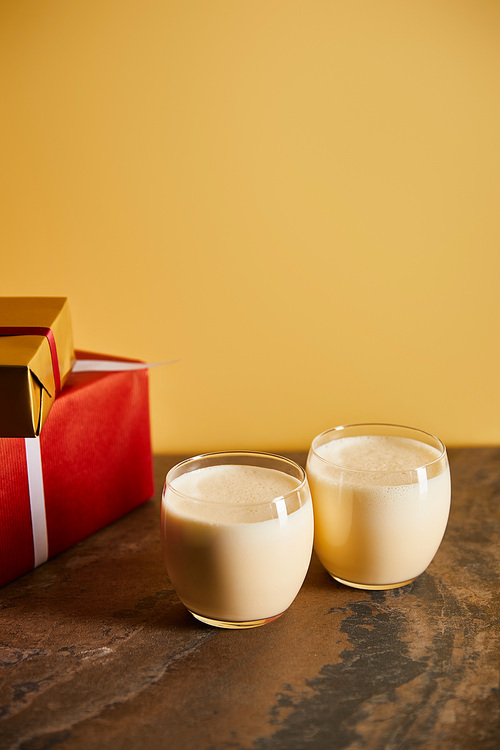 delicious eggnog cocktail and gift boxes on dark marble table isolated on orange