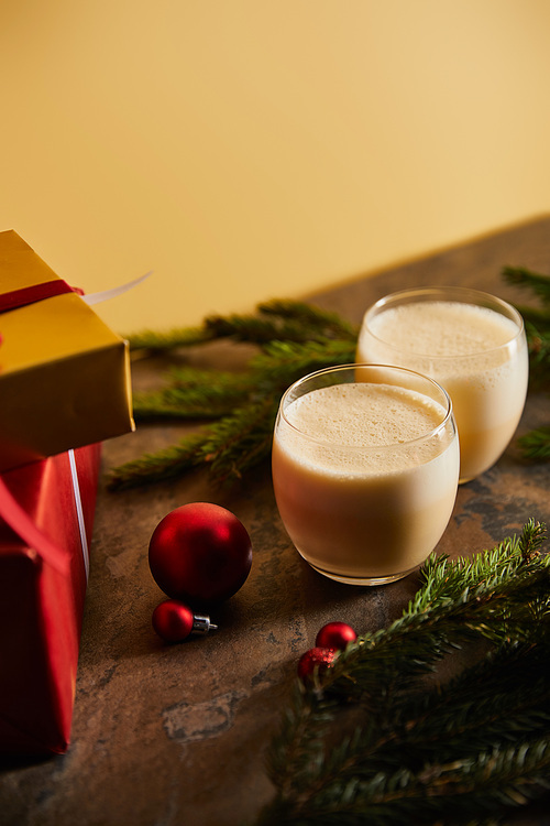 traditional eggnog cocktail, gift boxes, spruce branches and Christmas balls on dark marble table isolated on orange