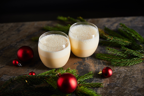 delicious eggnog cocktail, spruce branches and christmas balls on dark marble table isolated on black