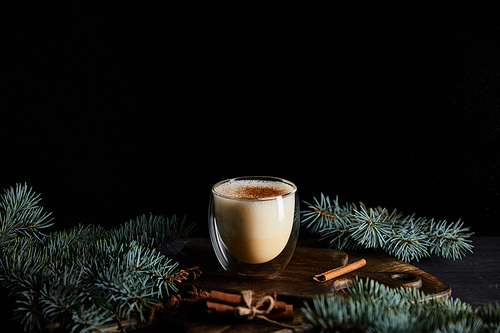 delicious eggnog cocktail on cutting board near spruce branches and cinnamon sticks isolated on black