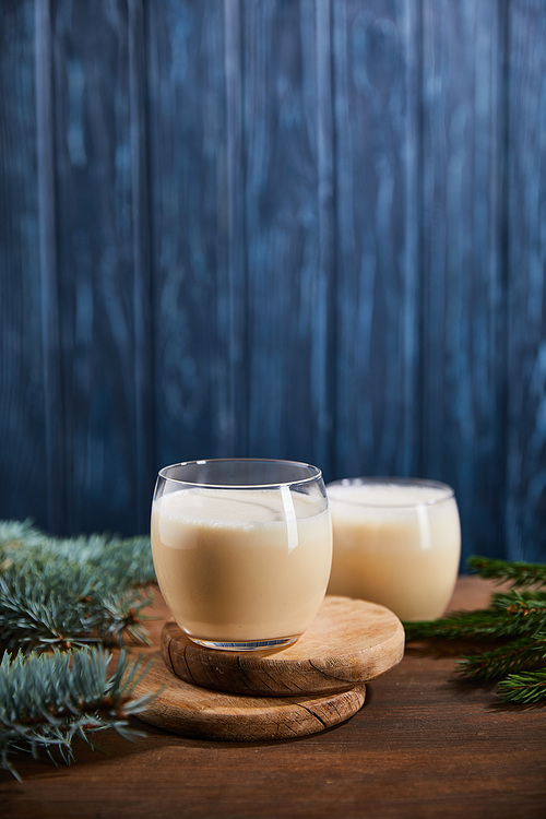 delicious eggnog cocktail on round wooden boards near spruce branches on blue textured background