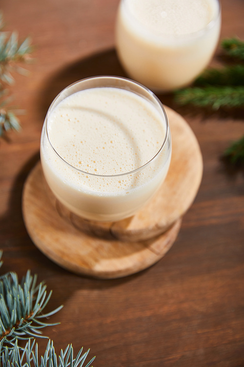 delicious eggnog cocktail on round wooden boards near spruce branches on wooden table