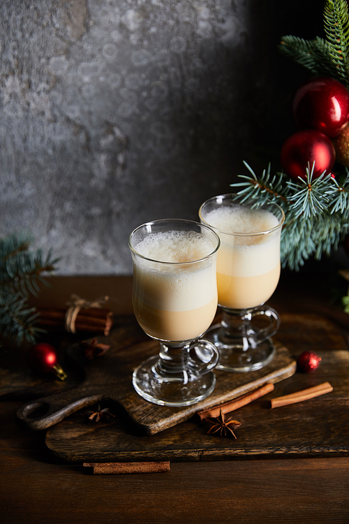traditional eggnog cocktail on cutting board near decorated spruce branches on grey stone background