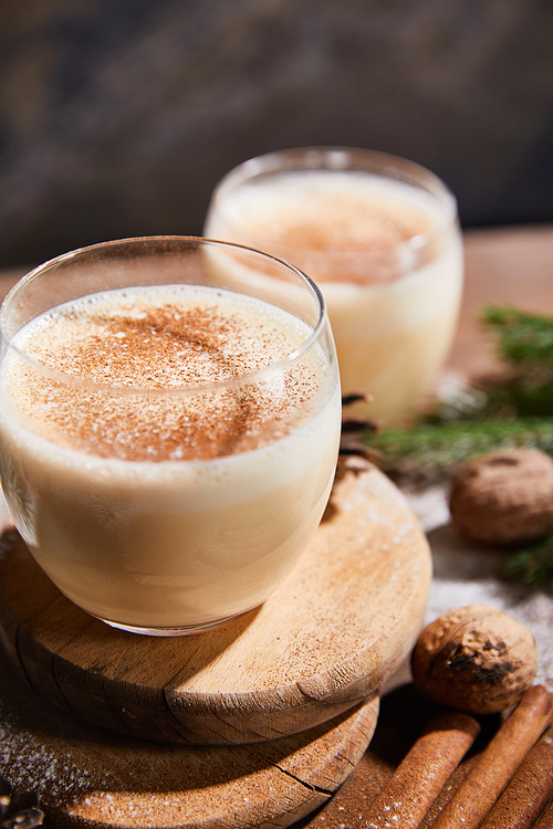 close up view of delicious eggnog cocktail on round boards, cinnamon sticks and walnuts on wooden table