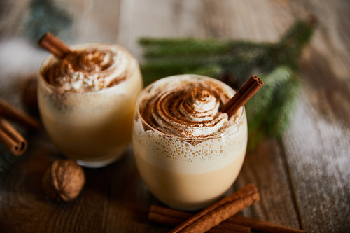 selective focus of delicious eggnog cocktail with whipped cream near cinnamon sticks on wooden table