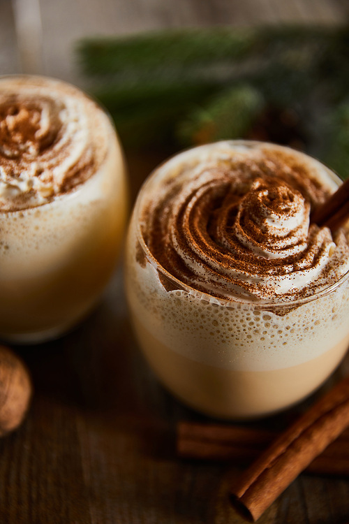 close up view of tasty eggnog drink with whipped cream and cinnamon on wooden table