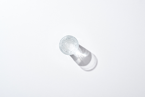 top view of transparent glass with water on white surface with shadow