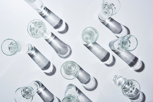 top view of transparent glasses with water on white background with shadows
