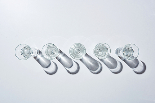 top view of transparent glasses with water in row on white background with shadows